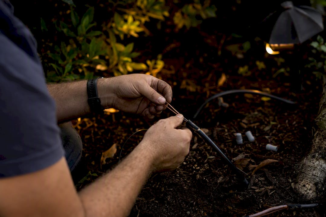 Landscape Lighting Cost: What U.S. Homeowners Pay in 2026 Hands inspecting landscape lighting cable in garden trench